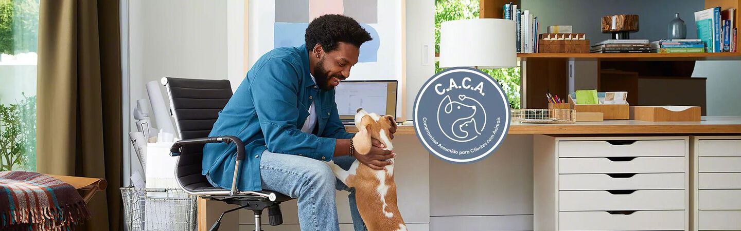 Um homem ao computador com um cão. Logótipo do Compromisso Assumido para Clientes com Animais